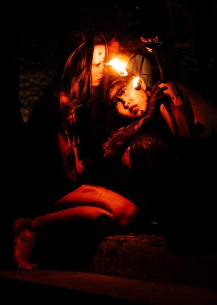 A performer lit by red light and handheld flame in a darkened church.