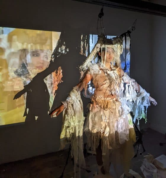 A draped, projection-lit figure installation in a dark room.