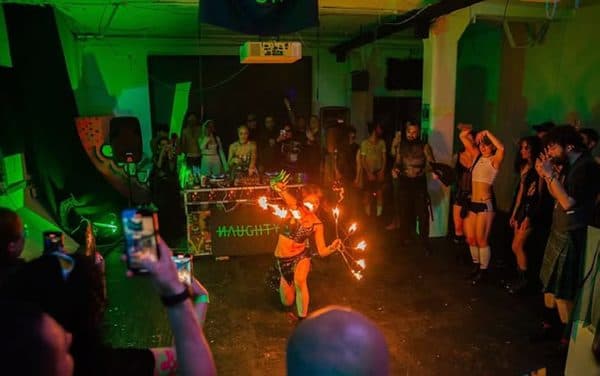 A fire performer spinning flames before a crowd under green light.