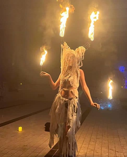A fire dancer in a feathered headpiece holding lit torches.