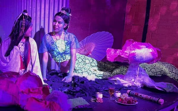 A performer in scaled costume under magenta light.
