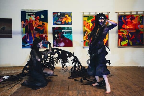 Performers in black amid a gallery hung with vivid paintings.